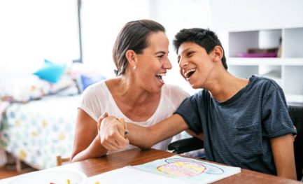 Mother and son laughing while they sit at a table working on therapy exercises